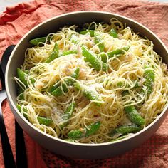 a white bowl filled with pasta and green beans on top of a red towel next to a fork