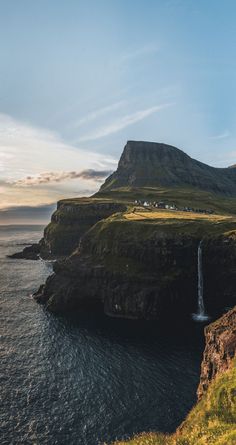 an island with a waterfall in the middle and green grass on both sides, surrounded by water