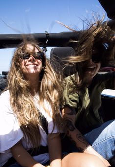 two women sitting in the back of a car with their hair blowing in the wind