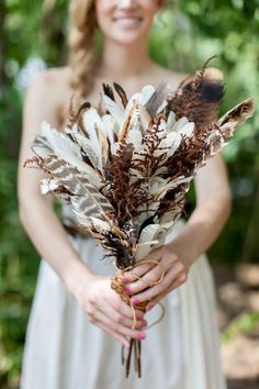 a woman in a white dress holding a bouquet of dried flowers and feathers on her hands