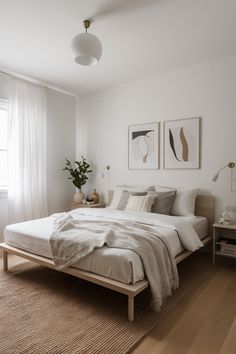 a bedroom with white walls and wood flooring has a large bed, two paintings on the wall