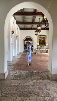 a woman in a blue robe is walking through an archway to a room with paintings on the walls