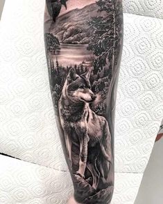 a man's leg with a wolf and mountain scene on the calf sleeve, done by