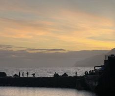 people are standing on the dock watching the sun go down over the water and mountains