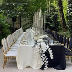 a long table is set with white flowers and black linens for an outdoor event