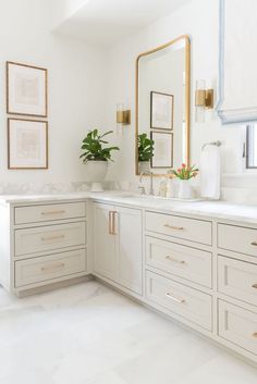 a bathroom with white cabinets and gold trim on the mirror above it is an indoor plant