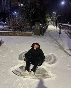 a man sitting on top of a snow covered ground next to a street light at night