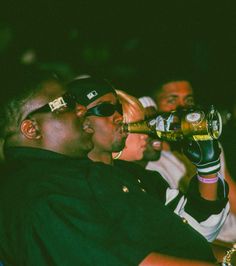 two men drinking beer while sitting next to each other in front of a group of people