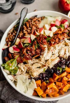 a white bowl filled with chicken, apples and cranberries next to a fork