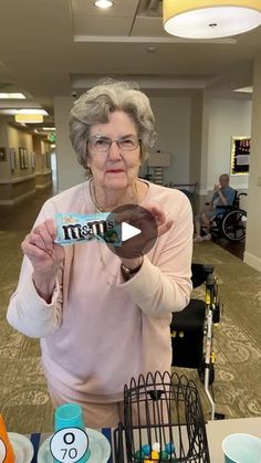 an older woman holding up a piece of chocolate in front of a table with other items