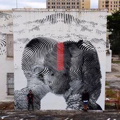 two people are standing in front of a large painting on the side of a building