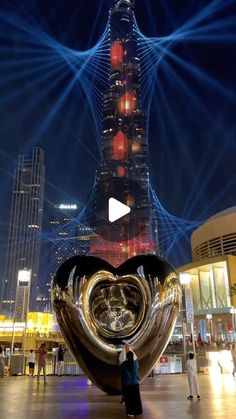 a person standing in front of a giant heart shaped object with lights on it's face