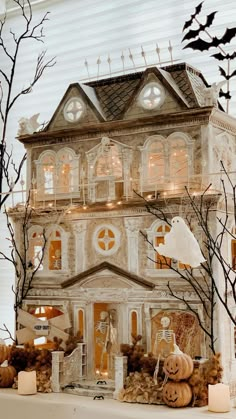 a halloween house with pumpkins and candles on the mantle in front of it, surrounded by fake trees