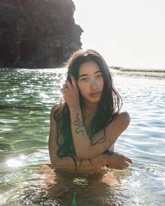 a woman sitting in the water with her arm around her head and holding a cell phone to her ear