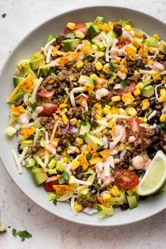 a white bowl filled with mexican salad and topped with lime wedges on the side