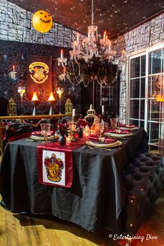 a dining room table set up for halloween with decorations on the wall and chandelier