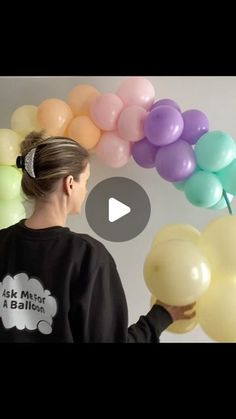 a woman is holding balloons in front of her face and looking at the balloon arch