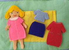 a doll laying on top of a green blanket next to two different pieces of clothing