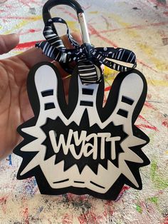 a hand holding a black and white keychain with the word wait on it