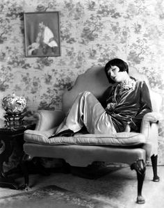 a woman sitting on top of a green chair in front of a wall with pink flowers