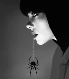 a black and white photo of a woman with a spider hanging from her mouth