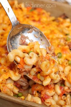 a spoon scooping some food out of a casserole dish with pasta and vegetables