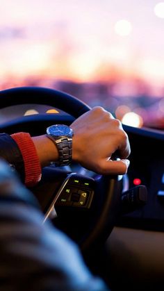 a man driving a car with his hand on the steering wheel while wearing a watch