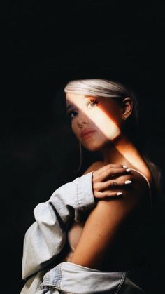 a woman with white hair and ring on her finger is looking at the camera while standing in front of a dark background