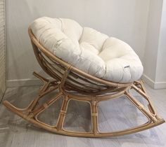 a wicker rocking chair with white cushions on the floor next to a wall in a room