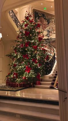 a decorated christmas tree in the middle of a room with stairs and paintings on the walls