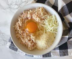 an egg and shredded cheese in a white bowl on a checkered cloth next to a black and white towel