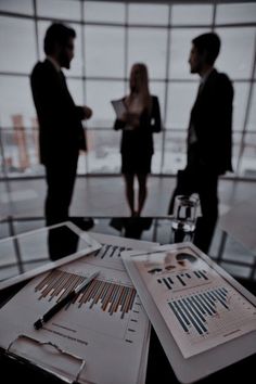 two people standing in an office with papers and pens on the table next to them