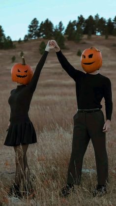 two people in costumes holding hands with pumpkins on their heads