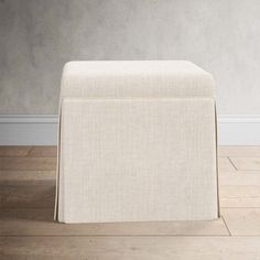 an upholstered footstool sits on the floor in front of a wall