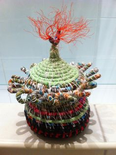 a hat made out of yarn and thread with an orange hair on top is sitting on a table