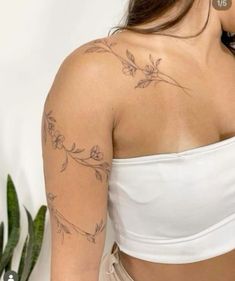 a woman with a tattoo on her arm and shoulder is standing in front of a potted plant