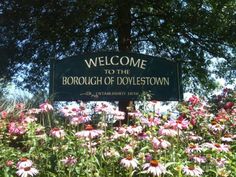 a welcome sign to the borough of doylestown surrounded by wildflowers and trees