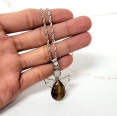 Introducing our Tiger's Eye Pendant Necklace, a simple yet elegant piece of jewelry that is perfect for everyday wear.The pendant features a beautiful Tiger's Eye stone in a silver-plated setting. You can choose from multiple stainless steel chain lengths or a black wax cord to customize your necklace to your preferred length.Tiger's Eye is believed to promote courage, strength, and protection. This necklace is perfect for anyone who wants to add a touch of natural beauty to their outfit or as a Eye Angel, Tigers Eye Crystal, Eye Pendant Necklace, Artisan Jewelry Necklaces, Crystal Angel, Tiger Eye Crystal, Angel Necklace, Crystal Angels, Angel Pendant