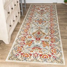 a white rug with red, orange and blue designs on it in a room next to a dresser