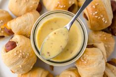 a spoon is in a jar filled with mustard and pigs in a blanket on a plate