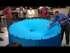 a man standing on top of a blue table next to other people in a room