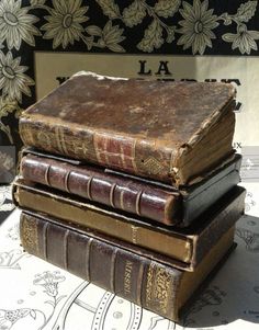 three old books stacked on top of each other in front of a floral wallpaper