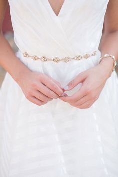 a woman in a white dress holding her hands together with a gold chain belt around her waist