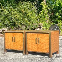 two wooden cabinets sitting next to each other on top of a gravel ground with trees in the background