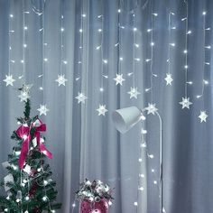 a small christmas tree with lights on it in front of a curtained room window