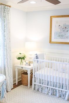 a baby's room with a white crib, blue curtains and a painting on the wall