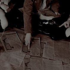 three people sitting on the floor looking at old newspapers with their hands pointing to them