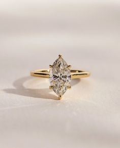 a yellow gold engagement ring with a pear shaped diamond in the center on a white surface