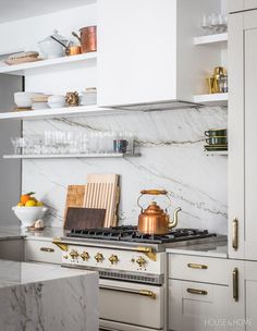 a kitchen with marble counter tops and gold accents on the stove top, along with white cabinets