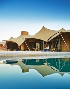 several tents are set up next to a pool with chairs and umbrellas on it